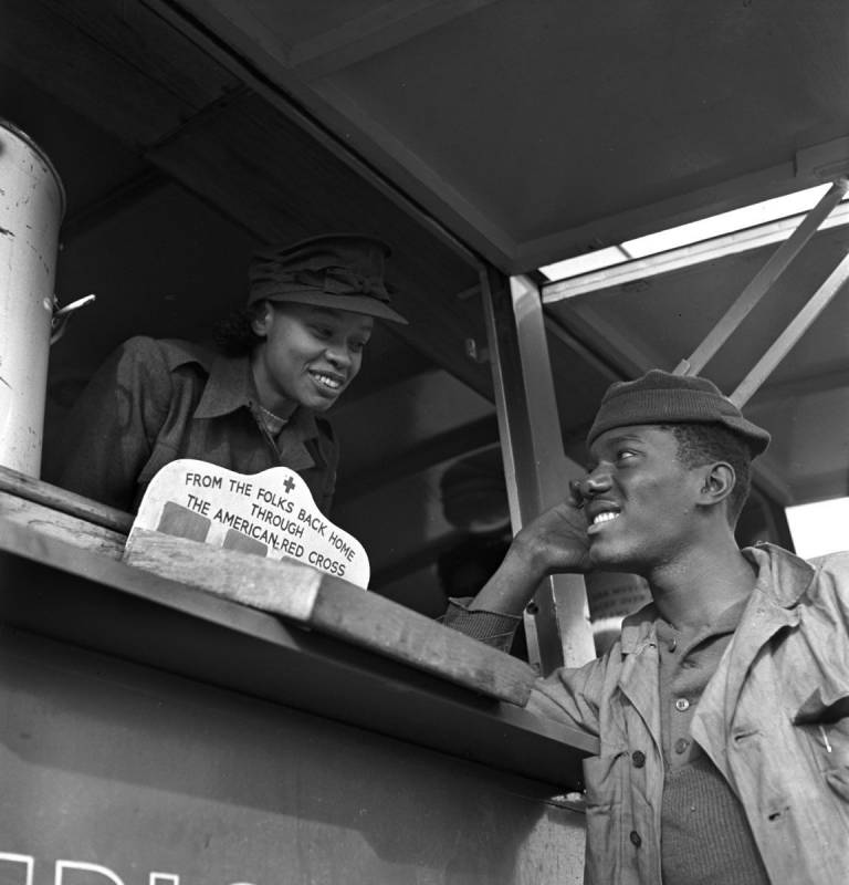 In historic photo, a female Red Crosser passes out coffee and doughnuts to soldiers.